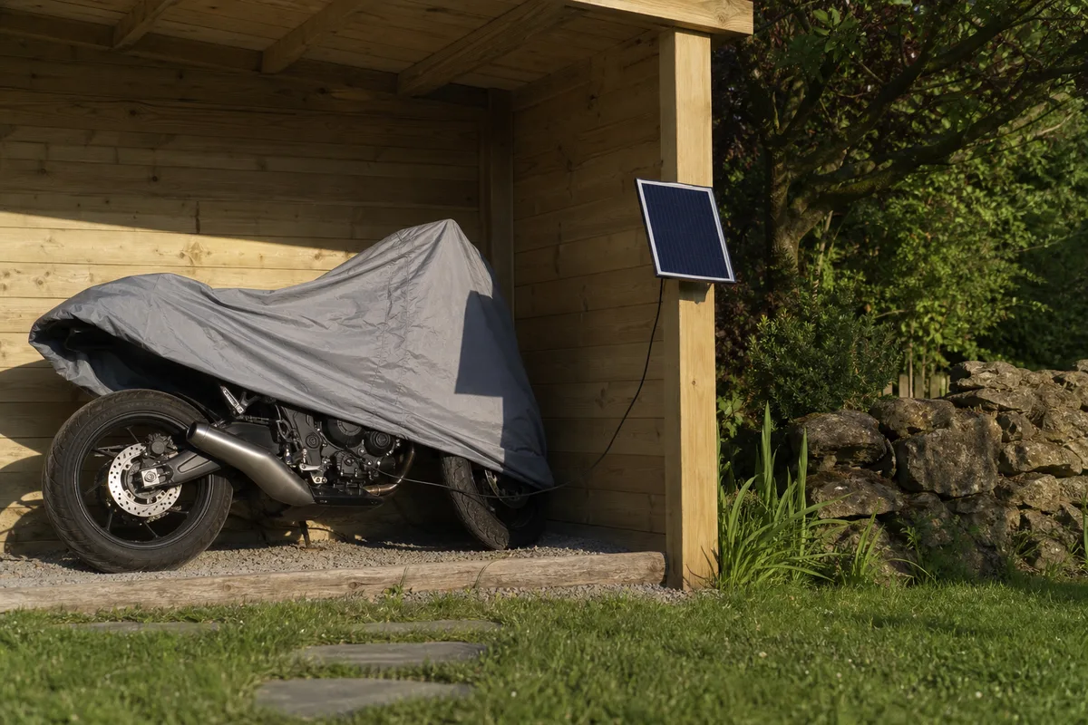 Petit panneau solaire de maintien relié à une moto stationnée sous un abri de jardin